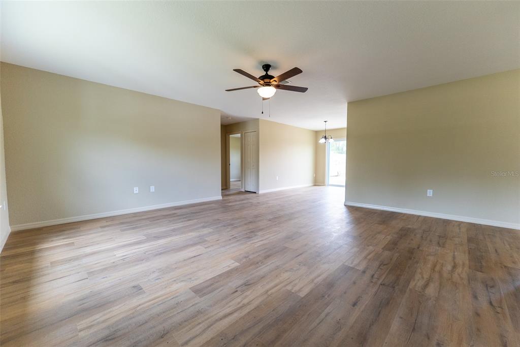 An open-concept living area features light-colored walls, wood-look flooring, and a ceiling fan — 487 MALAUKA RADIAL, OCKLAWAHA, FL