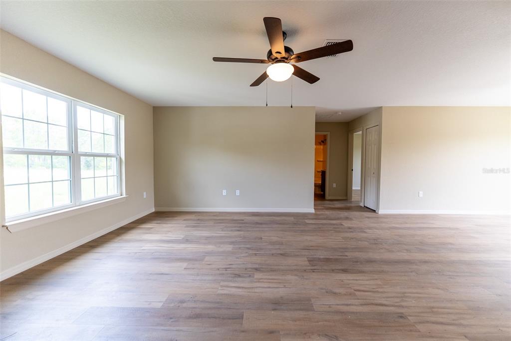 An empty room features light wood-look flooring, beige walls, a ceiling fan, and a large window — 487 MALAUKA RADIAL, OCKLAWAHA, FL