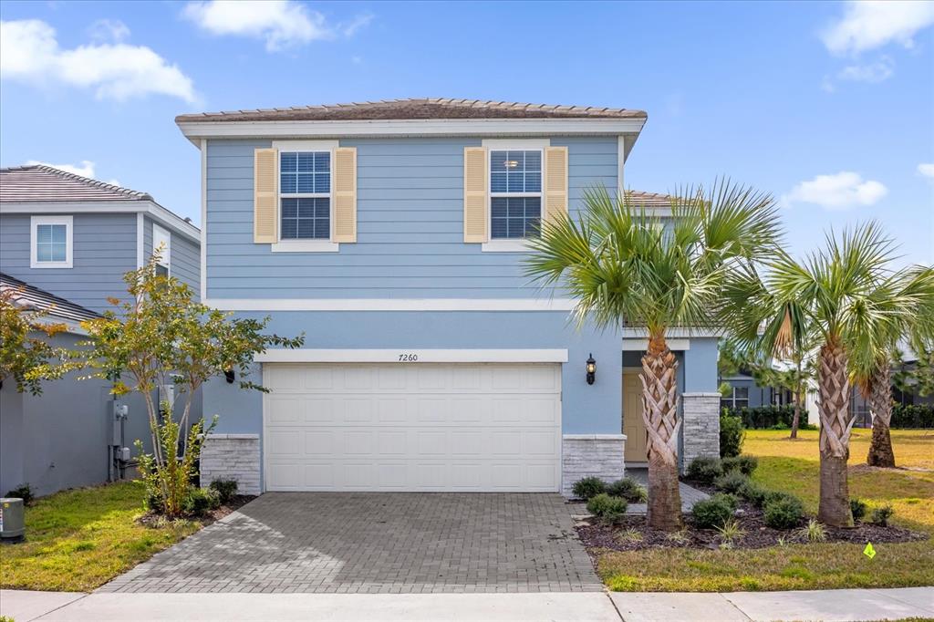 A two-story blue house features a white garage door, light shutters, and two palm trees — 7260 OAKMOSS LOOP, DAVENPORT, FL