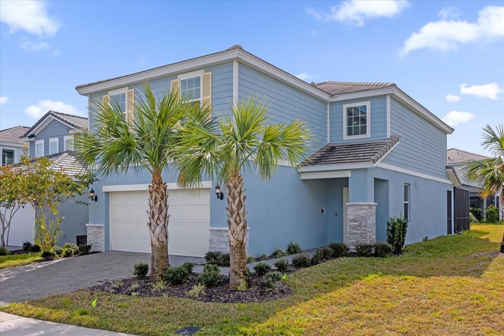A two-story blue house with a two-car garage, stone accents, and two palm trees — 7260 OAKMOSS LOOP, DAVENPORT, FL