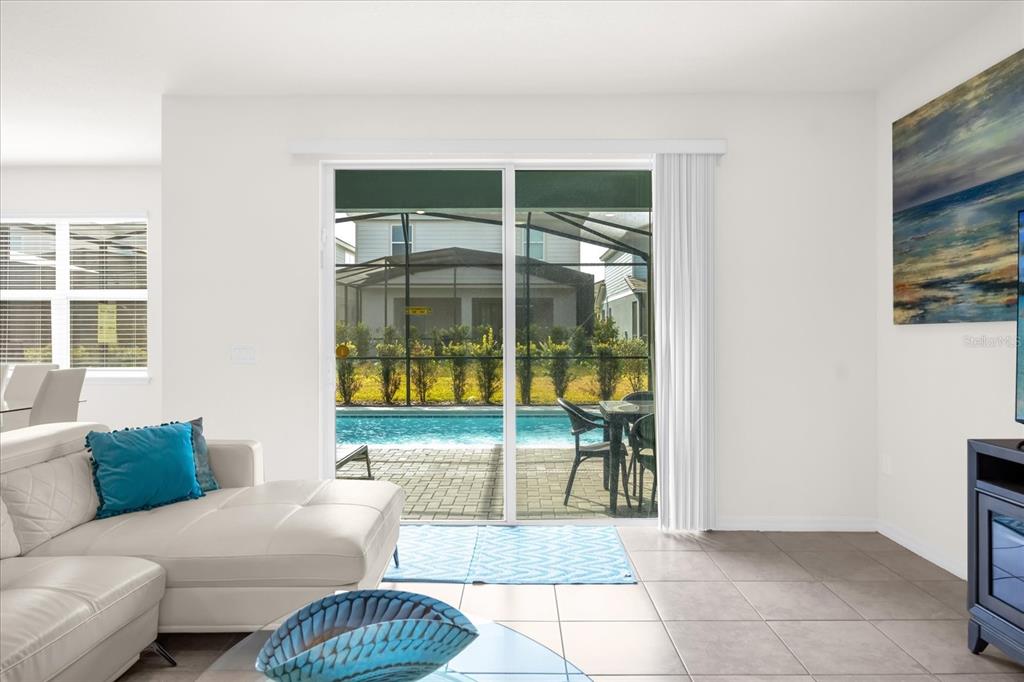 A living room with a white sectional sofa, tile floors, and sliding doors overlooking a pool — 7260 OAKMOSS LOOP, DAVENPORT, FL