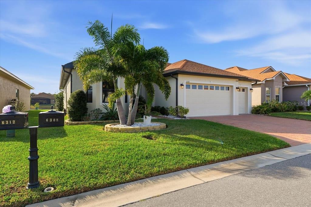 A single-story house with a tan exterior, a two-car garage, and a palm tree out front — 6308 PINEHURST LOOP, WINTER HAVEN, FL