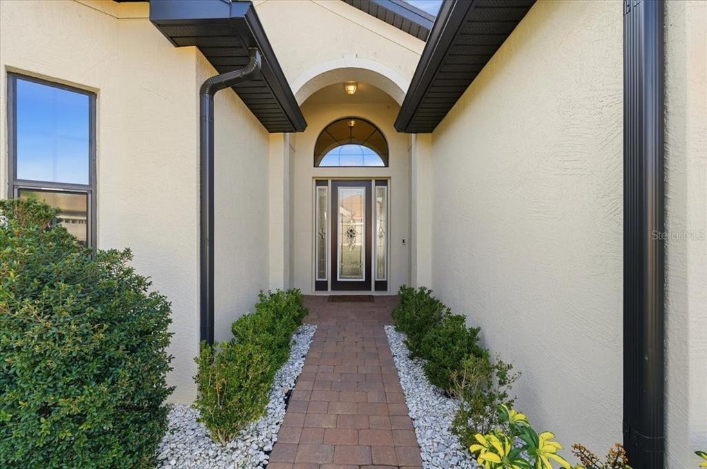 A paved walkway leads to the front entrance of a house with a glass door — 6308 PINEHURST LOOP, WINTER HAVEN, FL