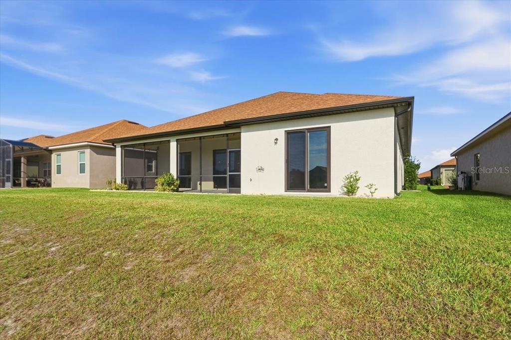 The back exterior of a single-story house features a screened-in lanai and a sliding door — 6308 PINEHURST LOOP, WINTER HAVEN, FL