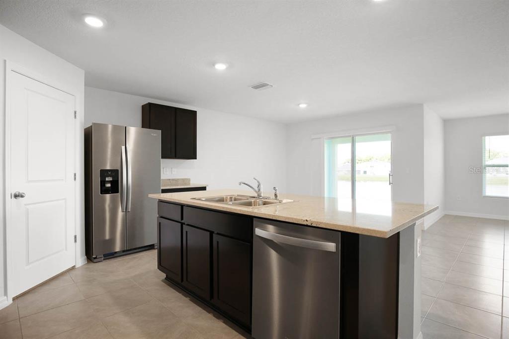 A kitchen features dark wood cabinets, granite countertops, a central island, and stainless steel appliances — 16530 WINDMILL FORGE PASS, WIMAUMA, FL