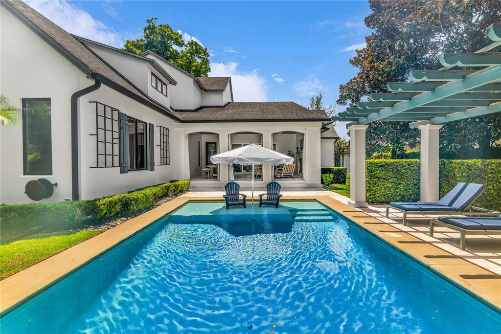 A swimming pool with a sun shelf and umbrella sits before a white house exterior — 1597 OAKHURST AVENUE, WINTER PARK, FL