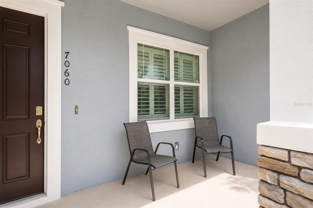 A covered front porch features a brown door, two gray chairs, and a window — 7060 VENTNOR DRIVE, WINDERMERE, FL