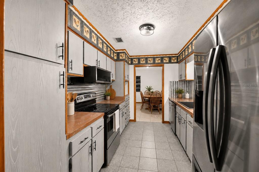 A galley kitchen features gray cabinets, stainless steel appliances, and a decorative rooster-themed wallpaper border — 101 ALLEN DRIVE, PALATKA, FL
