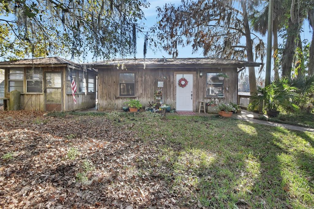 A rustic wooden cabin with a screened porch, a front door, and surrounding trees — 55512 FRONT STREET, ASTOR, FL