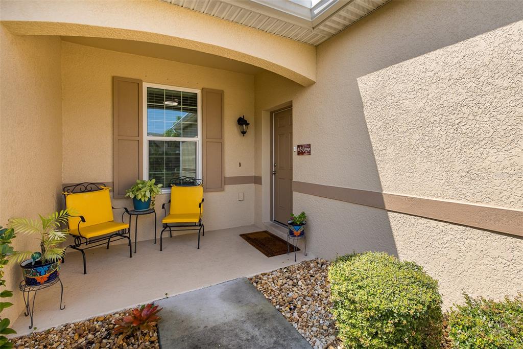 A covered front porch features two yellow chairs, a window with shutters, and landscaping — 2220 PARROT FISH DRIVE, HOLIDAY, FL