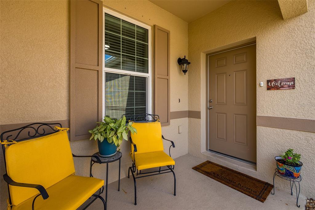 A covered front porch features two yellow chairs, a small table with a plant, and a door — 2220 PARROT FISH DRIVE, HOLIDAY, FL