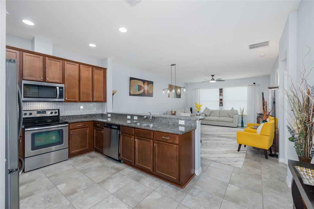 A kitchen with wood cabinets and granite countertops opens into a living room with seating — 2220 PARROT FISH DRIVE, HOLIDAY, FL