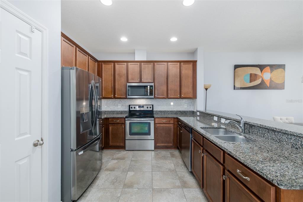 A kitchen with wood cabinets, stainless steel appliances, granite countertops, and tile flooring — 2220 PARROT FISH DRIVE, HOLIDAY, FL