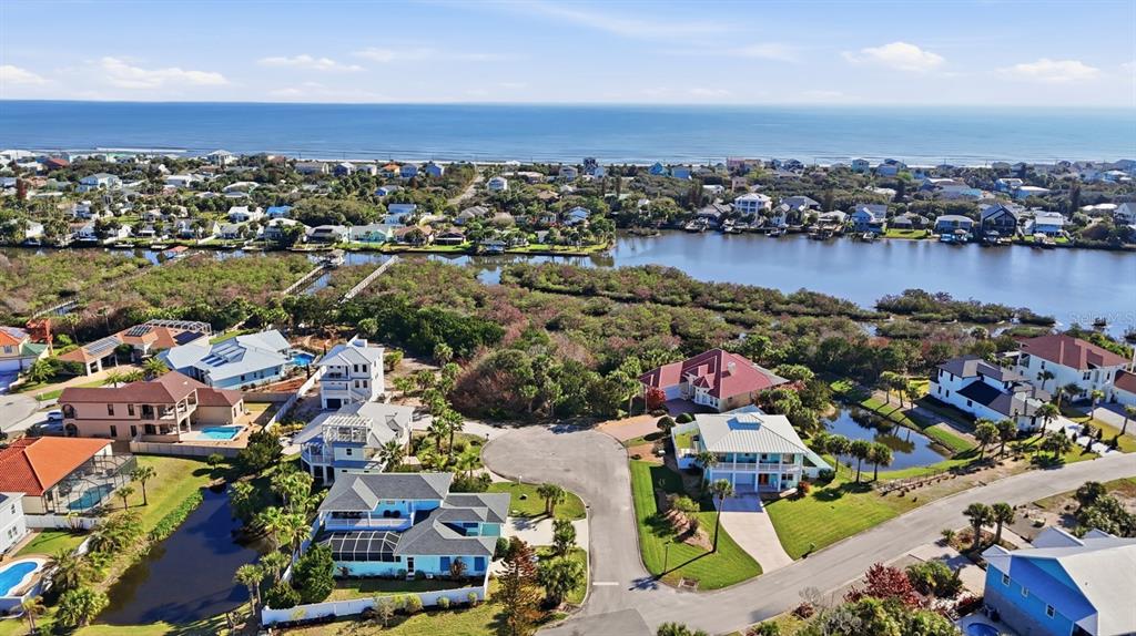 An aerial view shows a coastal neighborhood with houses, a waterway, and the ocean beyond — 570 SPRINGDALE DRIVE, FLAGLER BEACH, FL