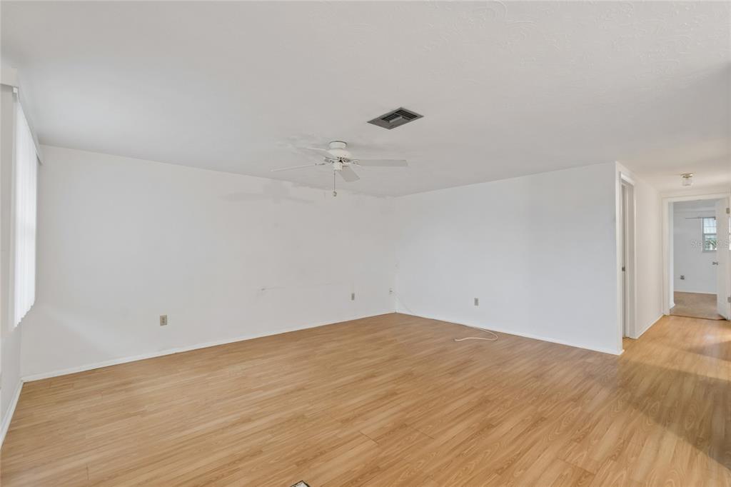 An empty room with light wood-look flooring, white walls, a ceiling fan, and a hallway — 3416 CHAUNCY ROAD, HOLIDAY, FL