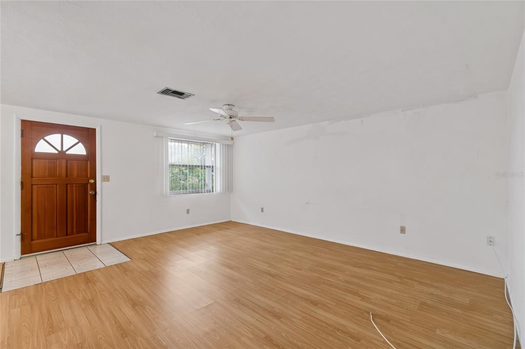 An empty room with light wood-look flooring, white walls, a ceiling fan, and a front door — 3416 CHAUNCY ROAD, HOLIDAY, FL
