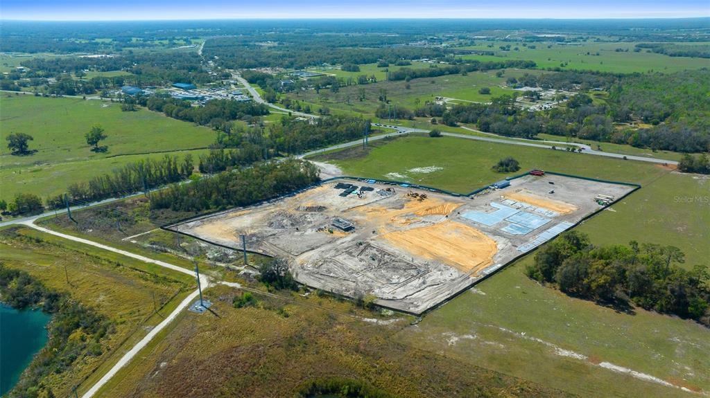 An aerial view shows a fenced construction site with cleared land and concrete building foundations — TBD 470 HIGHWAY, SUMTERVILLE, FL