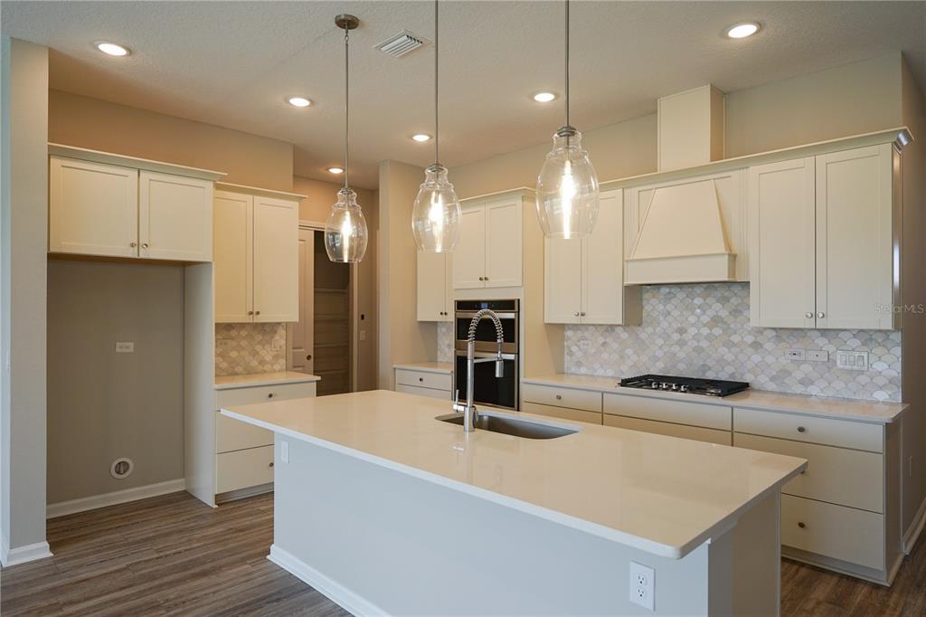 A kitchen features white cabinets, a quartz island with a sink, and a tiled backsplash — 282 KNOTTED BIRCH AVENUE, ST AUGUSTINE, FL