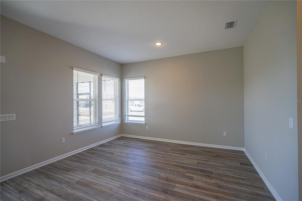 An empty room features light gray walls, wood-look flooring, and three windows with white blinds — 282 KNOTTED BIRCH AVENUE, ST AUGUSTINE, FL