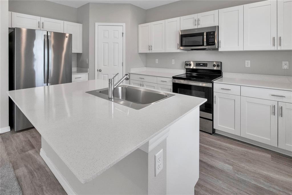 A kitchen features white cabinets, stainless steel appliances, a center island, and light-colored countertops — 12737 TANNENCREST DRIVE, RIVERVIEW, FL