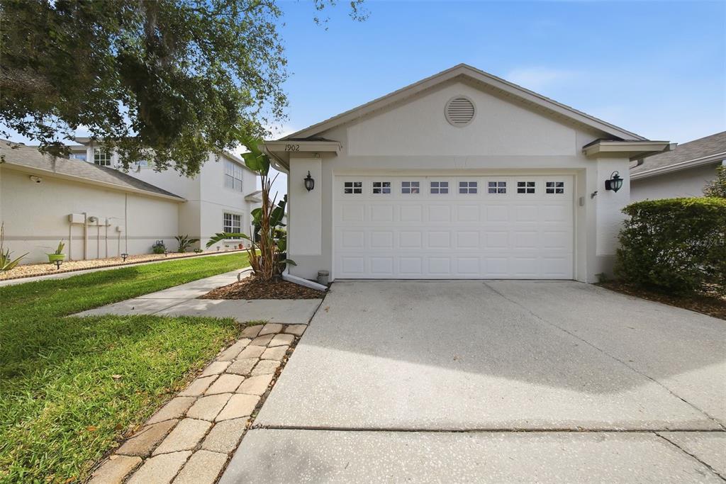 A white one-story house exterior features a two-car garage, a concrete driveway, and landscaping — 1902 ECHO POND PLACE, WESLEY CHAPEL, FL