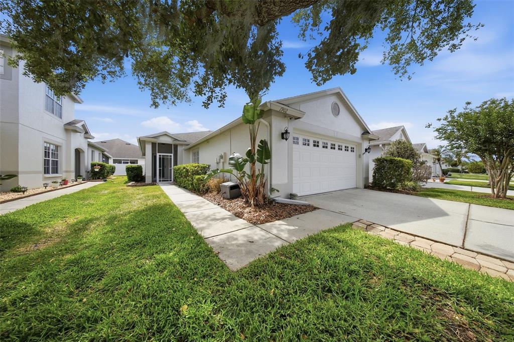 A single-story house with a white garage, a concrete walkway, and a landscaped front yard — 1902 ECHO POND PLACE, WESLEY CHAPEL, FL