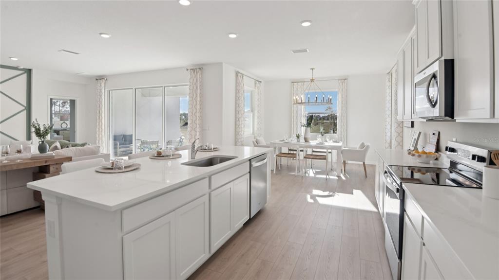 A modern kitchen with white cabinetry and a large island overlooks a bright dining area — 12760 NW 17TH PLACE, NEWBERRY, FL