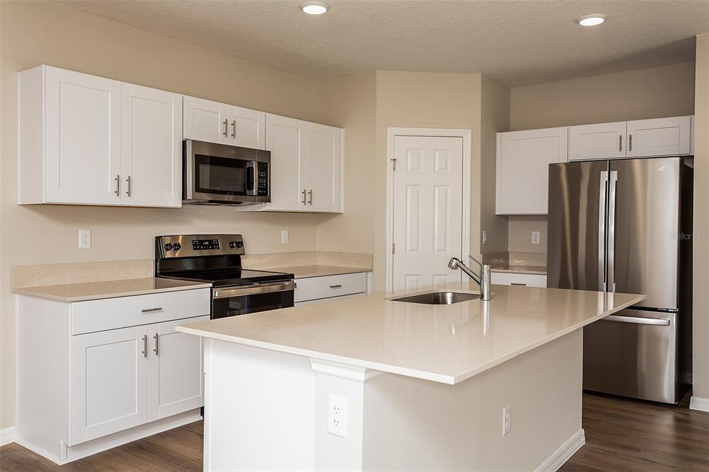 A kitchen features white cabinets, stainless steel appliances, a center island, and light countertops — 9092 BELLEVIEW FOREST PASS, DADE CITY, FL