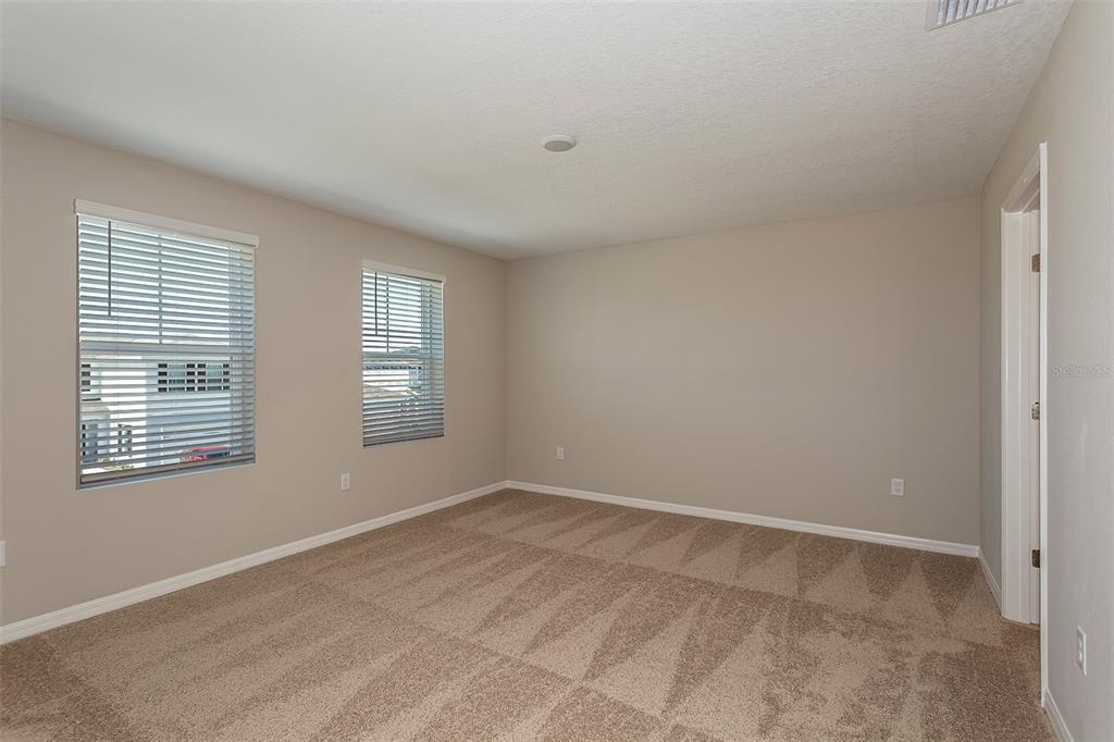An empty bedroom features beige walls, tan carpet, two windows with blinds, and a doorway — 9092 BELLEVIEW FOREST PASS, DADE CITY, FL
