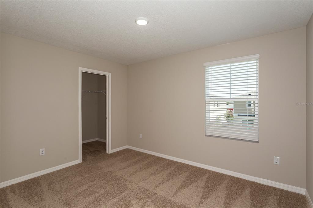 An empty bedroom features beige walls, tan carpeting, a window with blinds, and a closet — 9092 BELLEVIEW FOREST PASS, DADE CITY, FL