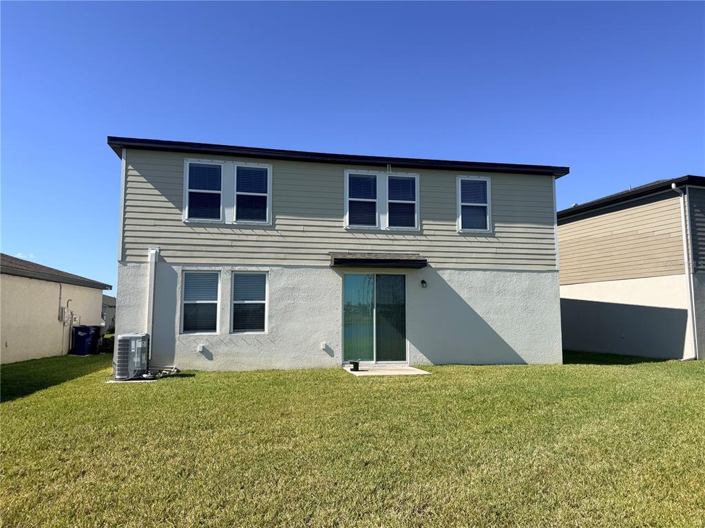 The rear exterior of a two-story house features light-colored siding, stucco, and a sliding door — 10062 DAYBREAK GLEN, PARRISH, FL