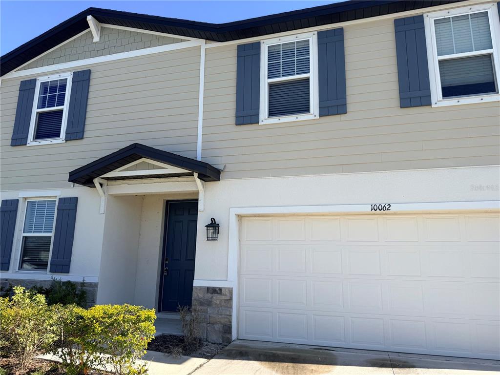A two-story suburban home features beige siding, blue shutters, a white garage, and stone accents — 10062 DAYBREAK GLEN, PARRISH, FL
