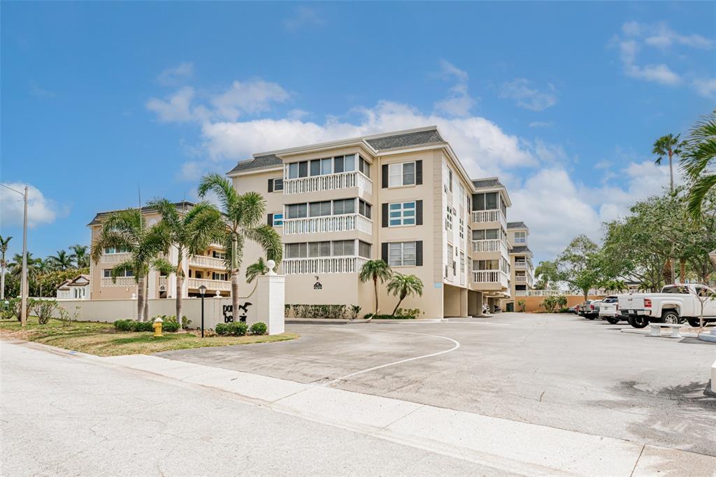 A multi-story apartment building features screened balconies, a parking lot, and surrounding palm trees — 147 BLUFF VIEW DRIVE UNIT 206, BELLEAIR BLUFFS, FL