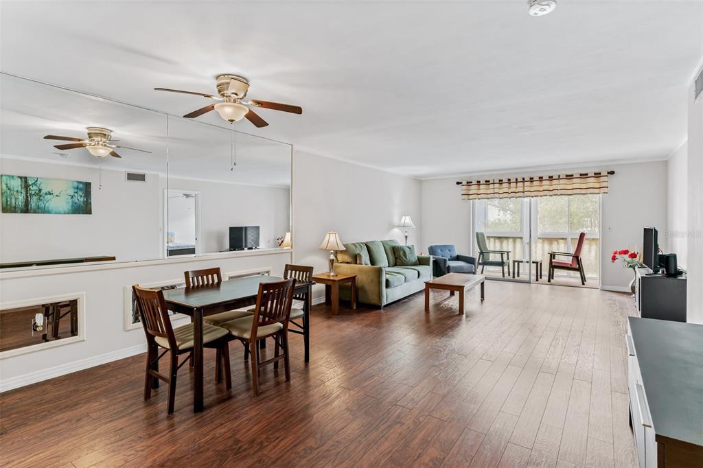 An open-concept living and dining area features wood-look flooring, a mirrored wall, and sliding doors — 147 BLUFF VIEW DRIVE UNIT 206, BELLEAIR BLUFFS, FL
