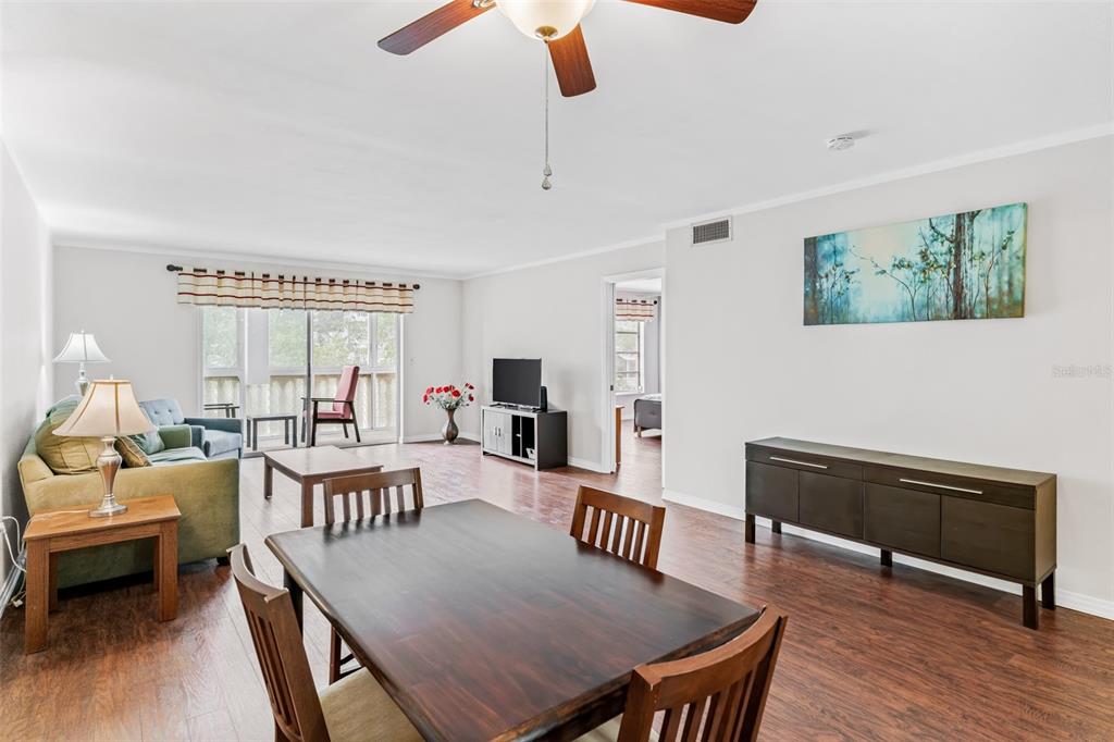 A living and dining area with wood-look flooring, a ceiling fan, and a sliding glass door — 147 BLUFF VIEW DRIVE UNIT 206, BELLEAIR BLUFFS, FL