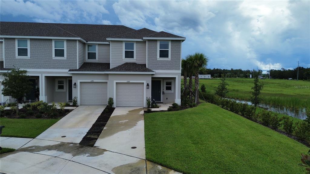 A two-story townhouse with a two-car garage and a grassy yard beside a pond — 2287 PORTRAIT STREET, KISSIMMEE, FL
