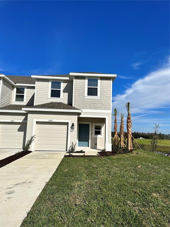 A two-story townhouse exterior features a beige facade, a single-car garage, and a blue front door — 2287 PORTRAIT STREET, KISSIMMEE, FL