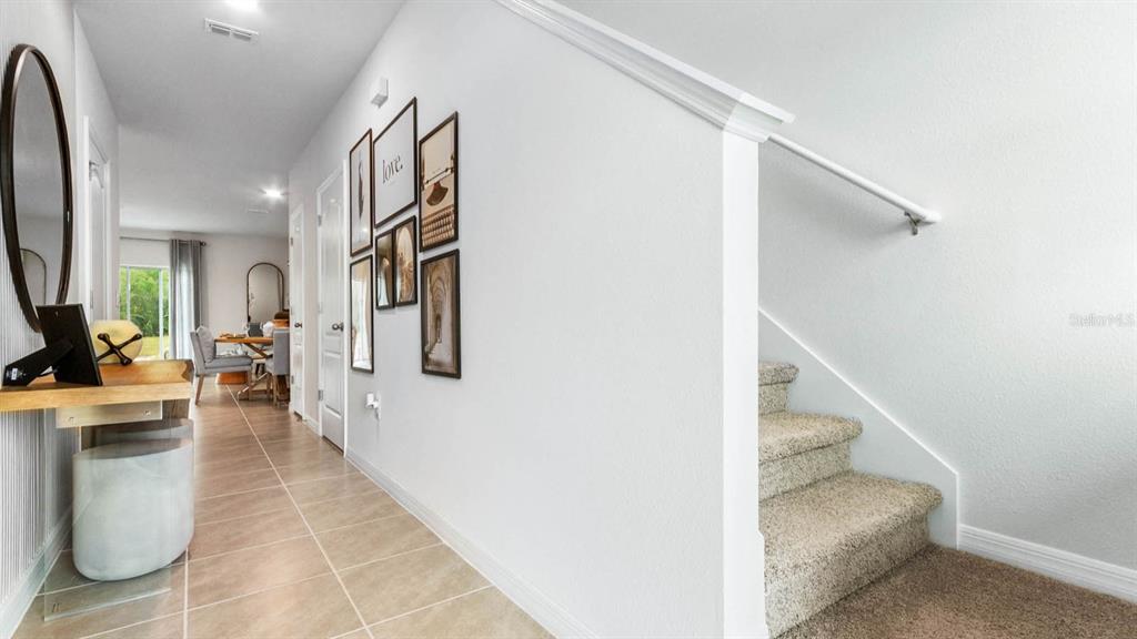 A hallway with tile floors, a staircase with carpet, and framed wall art — 931 SPOTTED EGRET LOOP, RUSKIN, FL