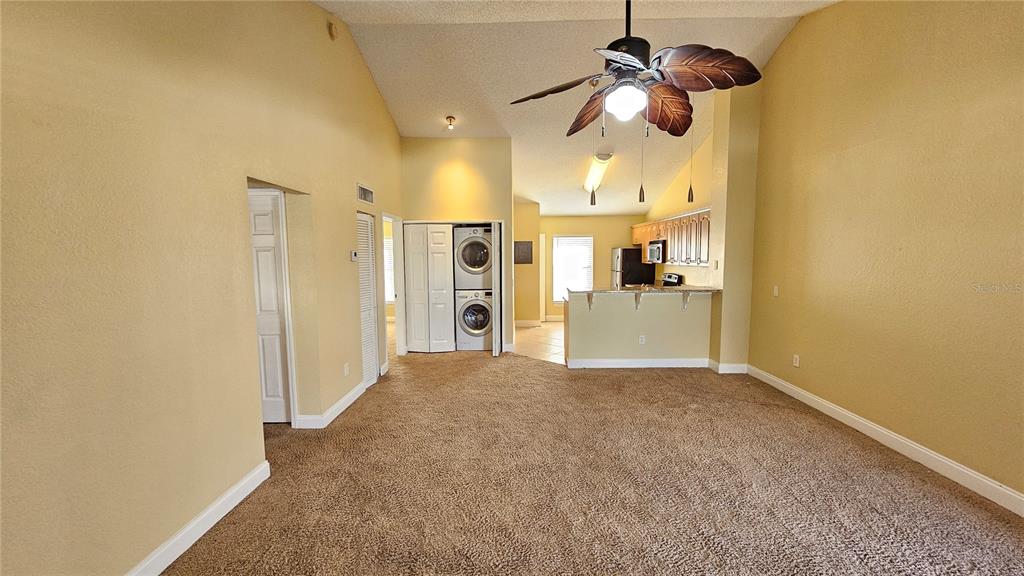 A living room with tan carpet and vaulted ceilings leads to an open kitchen area — 3651 N GOLDENROD ROAD UNIT C205, WINTER PARK, FL