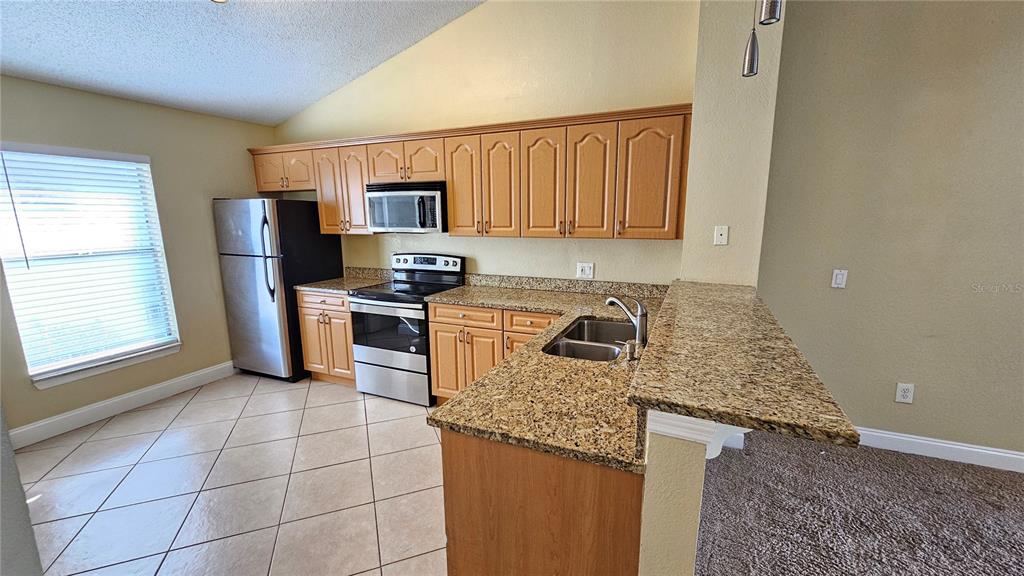 A kitchen features light wood cabinets, granite countertops, stainless steel appliances, and tile flooring — 3651 N GOLDENROD ROAD UNIT C205, WINTER PARK, FL