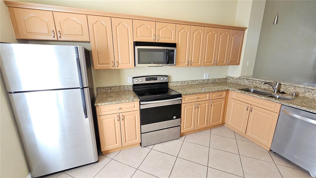 A kitchen features light wood cabinets, granite countertops, and stainless steel appliances over tiled floors — 3651 N GOLDENROD ROAD UNIT C205, WINTER PARK, FL