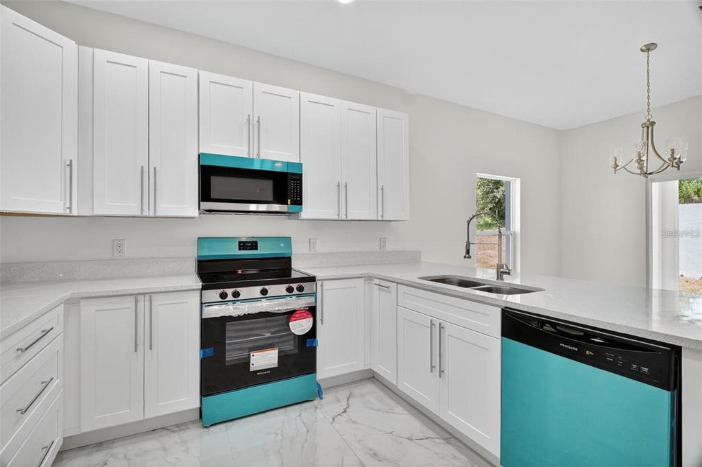 A kitchen with white cabinets, quartz countertops, marble-look floors, and teal-accented appliances — 89 FARIWAY CIRCLE, UMATILLA, FL