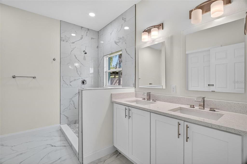 A bathroom features a double vanity with white cabinets, marble-look tile, and a walk-in shower — 89 FARIWAY CIRCLE, UMATILLA, FL