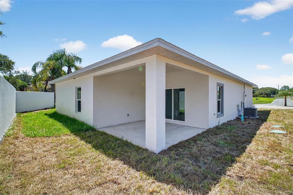 The exterior of a house features a covered concrete patio and a small backyard — 89 FARIWAY CIRCLE, UMATILLA, FL
