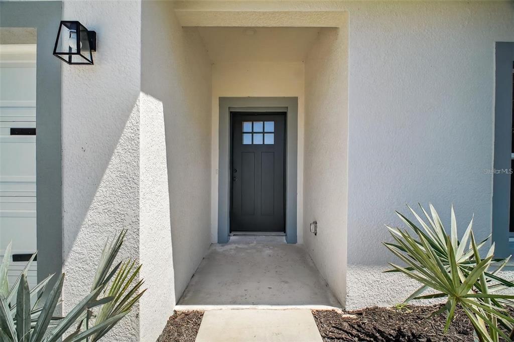 A dark front door with a window sits within a recessed entryway of a home — 89 FARIWAY CIRCLE, UMATILLA, FL