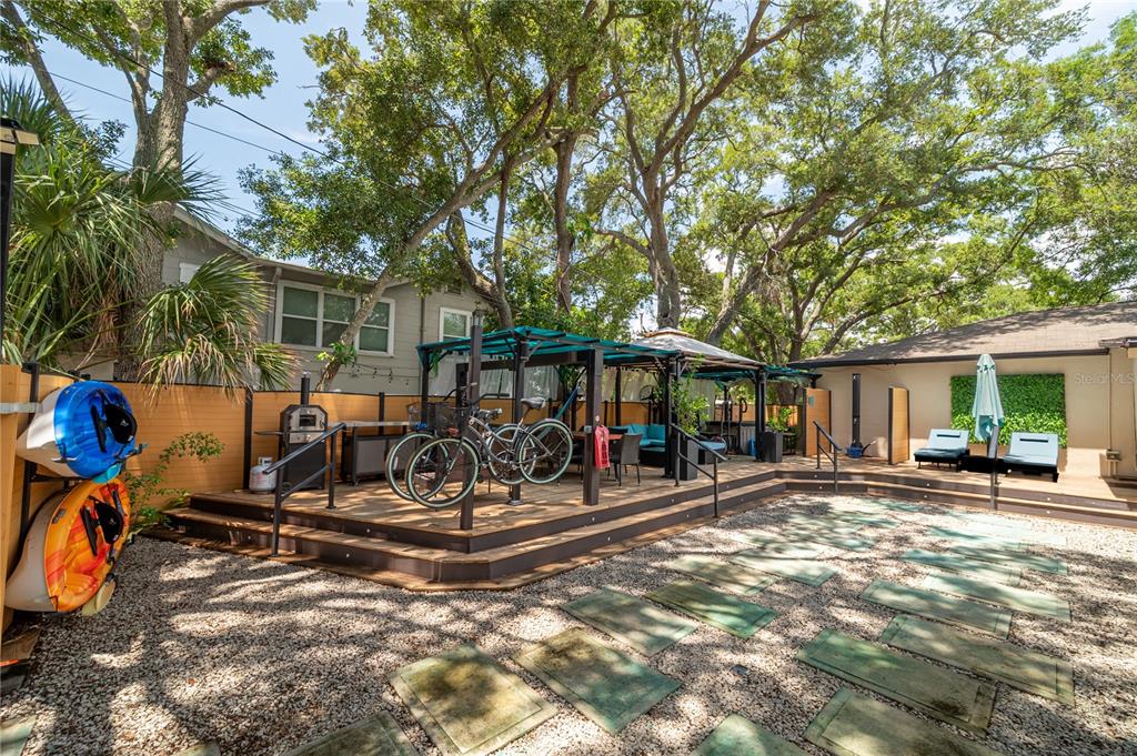 A backyard features a wooden deck with a pergola, bicycles, and a gravel patio area — 7410 5TH AVENUE N, ST PETERSBURG, FL