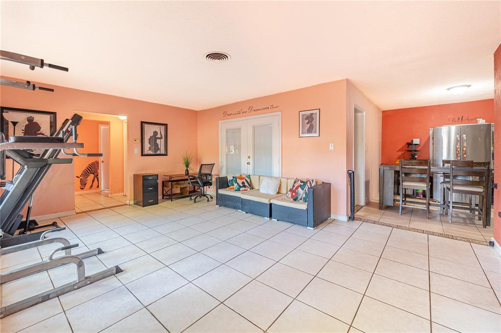 A spacious room with peach walls, white tile flooring, a home gym, and a dining area — 7410 5TH AVENUE N, ST PETERSBURG, FL