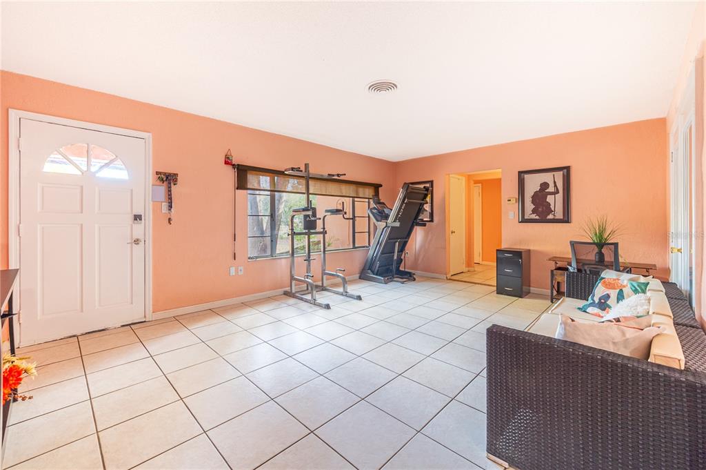 A room with peach walls, white tile floors, a workout station, and a wicker sofa — 7410 5TH AVENUE N, ST PETERSBURG, FL