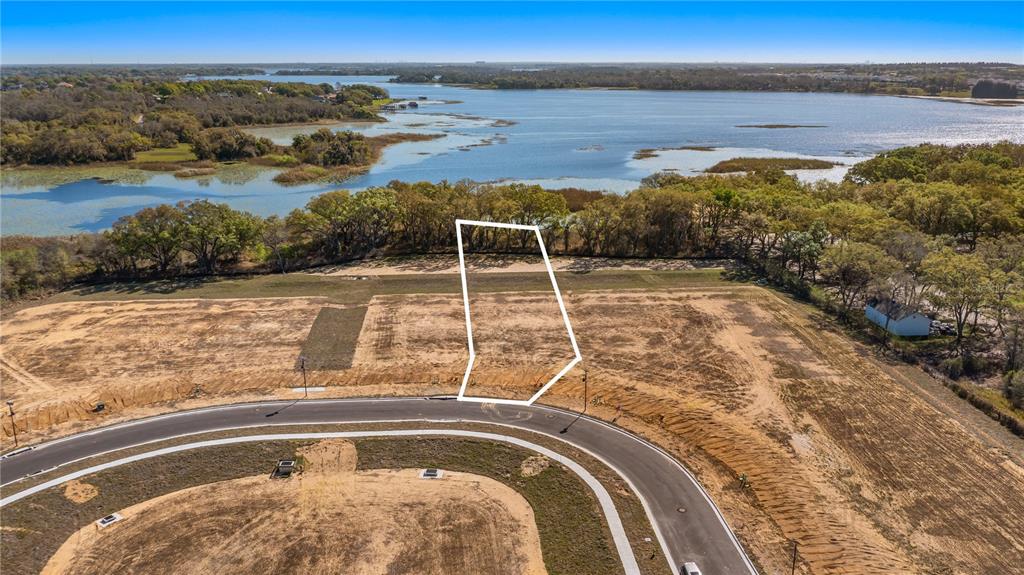 An aerial view shows a vacant, outlined residential lot bordering a lake and a curved road — MARIGOLD BELLE CIRCLE, CLERMONT, FL
