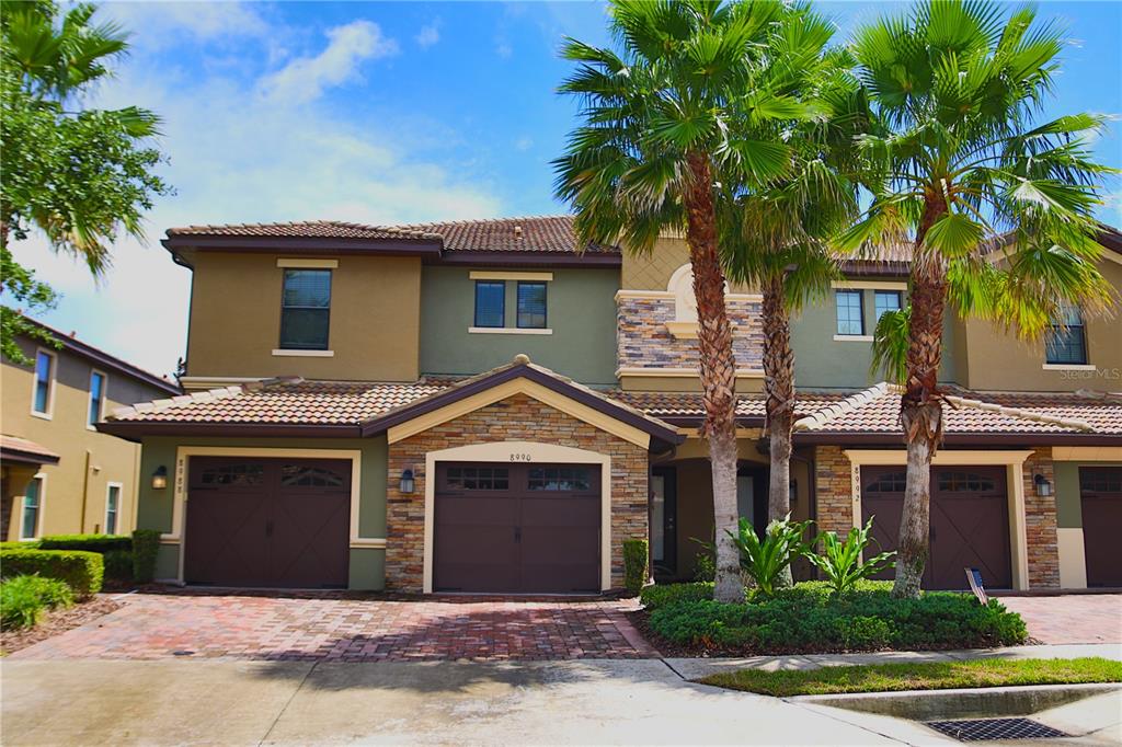 A two-story townhouse with a stone facade, brown garage doors, and palm trees in front — 8990 AZALEA SANDS LANE, DAVENPORT, FL